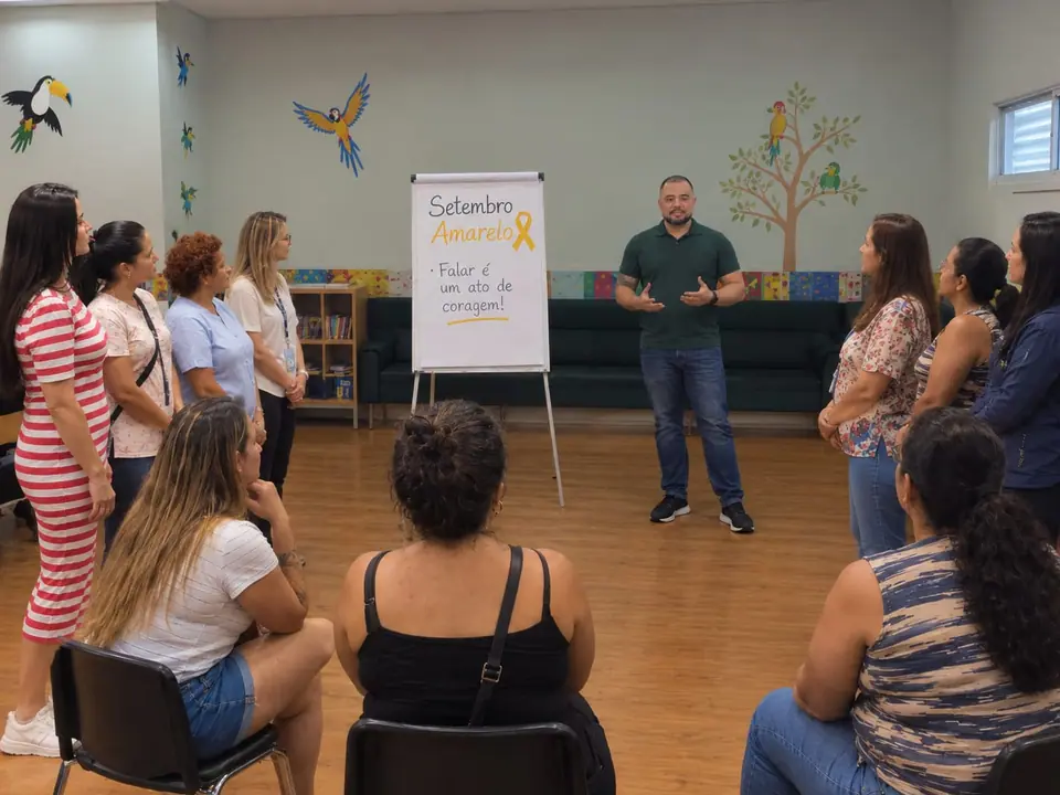 Diego Armando dando uma palestra do Setembro Amarelo para um grupo, ao lado do cartaz Falar é um ato de coragem